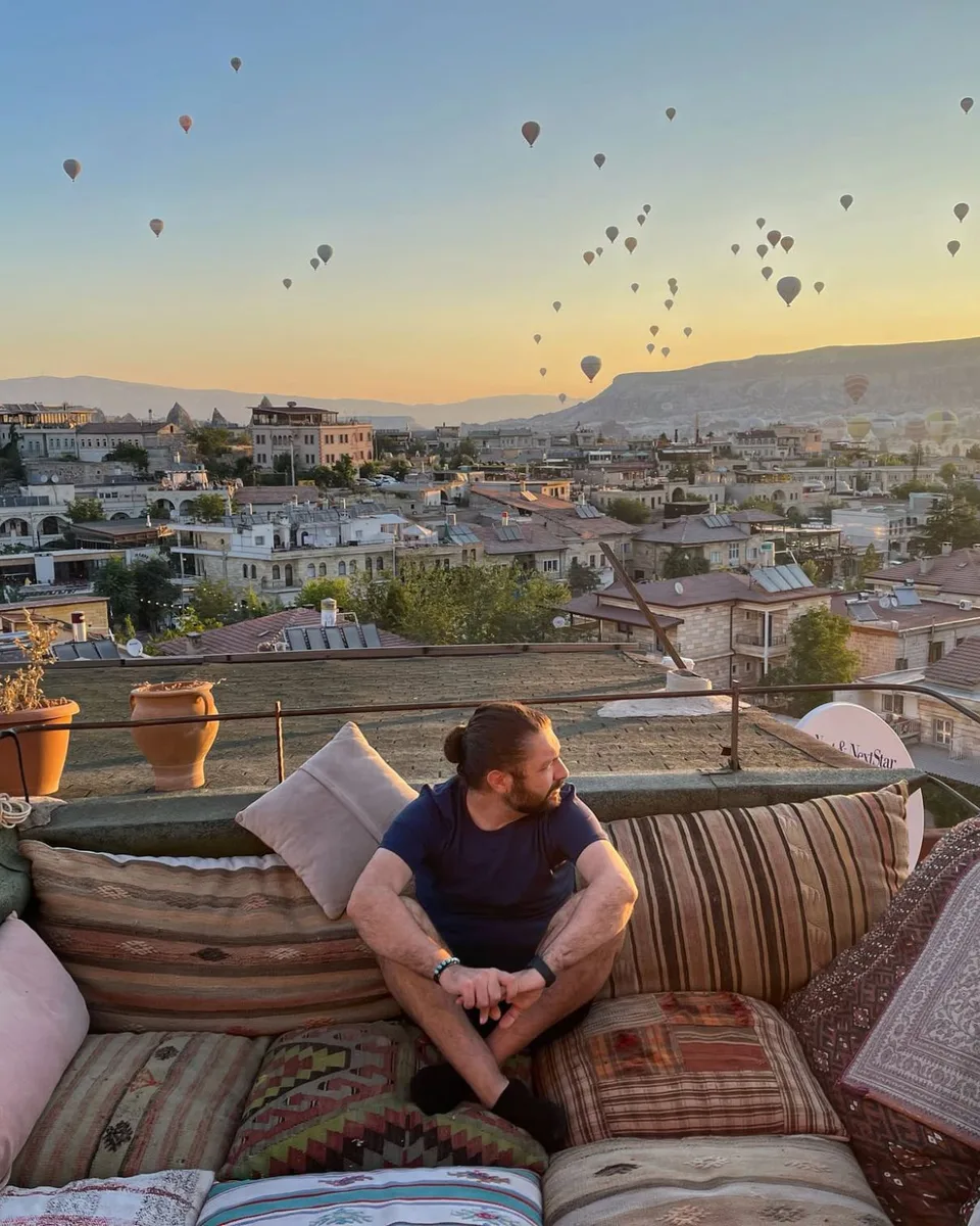 夜明けのカッパドキアの屋上に座るリッカルド・フィリッポーネ。空には熱気球